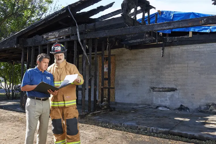 A Disaster Kleenup employee talking with a fire fighter in front of a fire damaged home